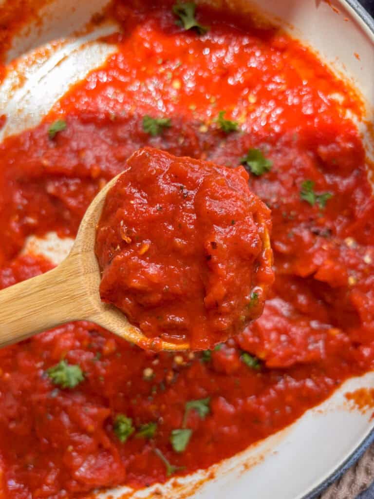 a wooden spoonful of spicy marinara sauce held over the pan of sauce