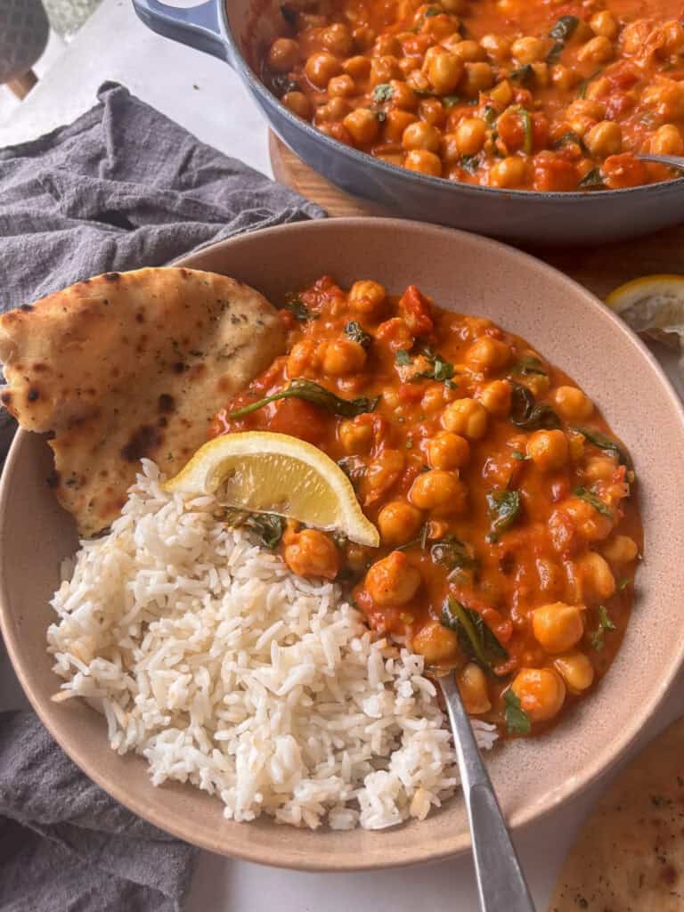 a bowl of chickpea and spinach curry with basmati rice and a lemon slice