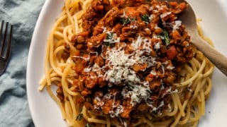 lentil bolognese served onto of spaghetti with cheese and fresh herbs topping with bolognese