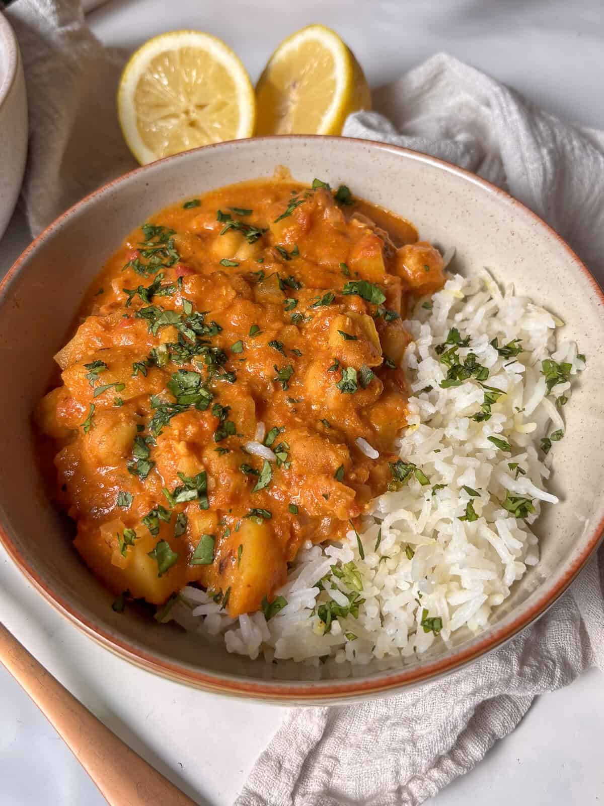a bowl of chickpea and potato curry, served with white rice and topped with cilantro