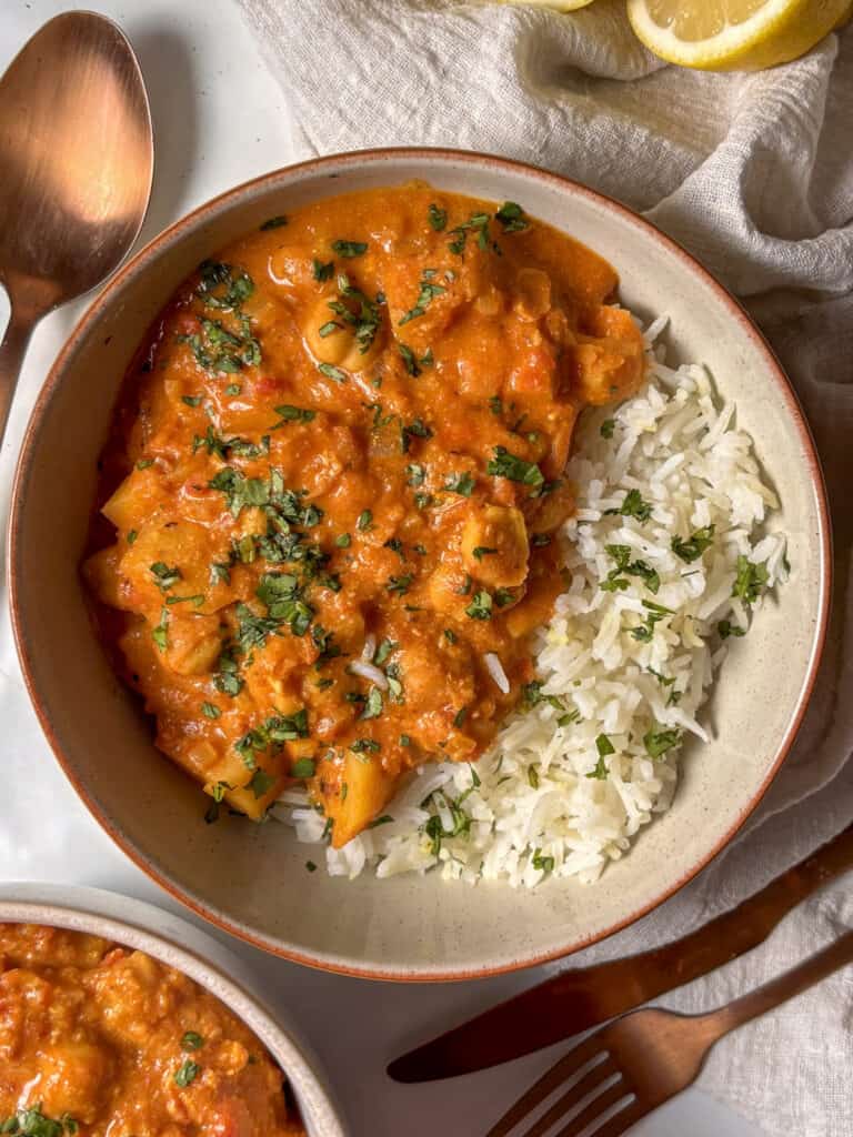 a bowl of chickpea and potato curry, served with white rice and topped with cilantro