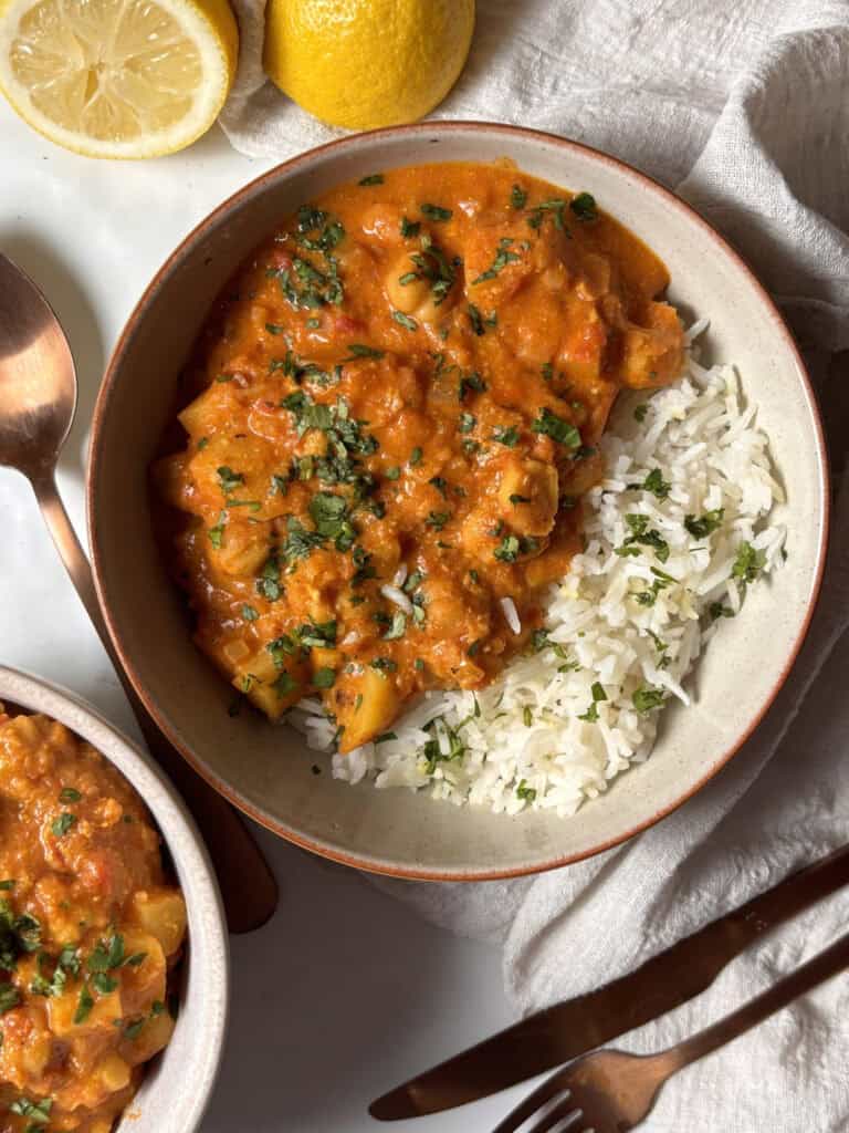 a bowl of chickpea and potato curry, served with white rice and topped with cilantro