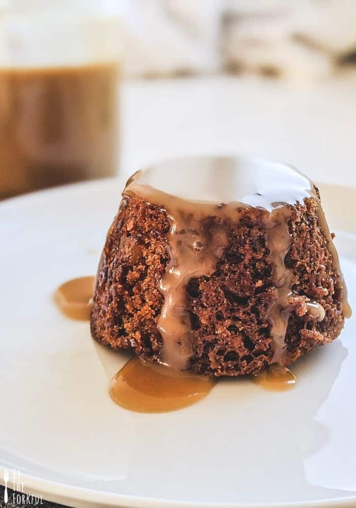 Sticky toffee pudding on a white plate, covered with toffee sauce.