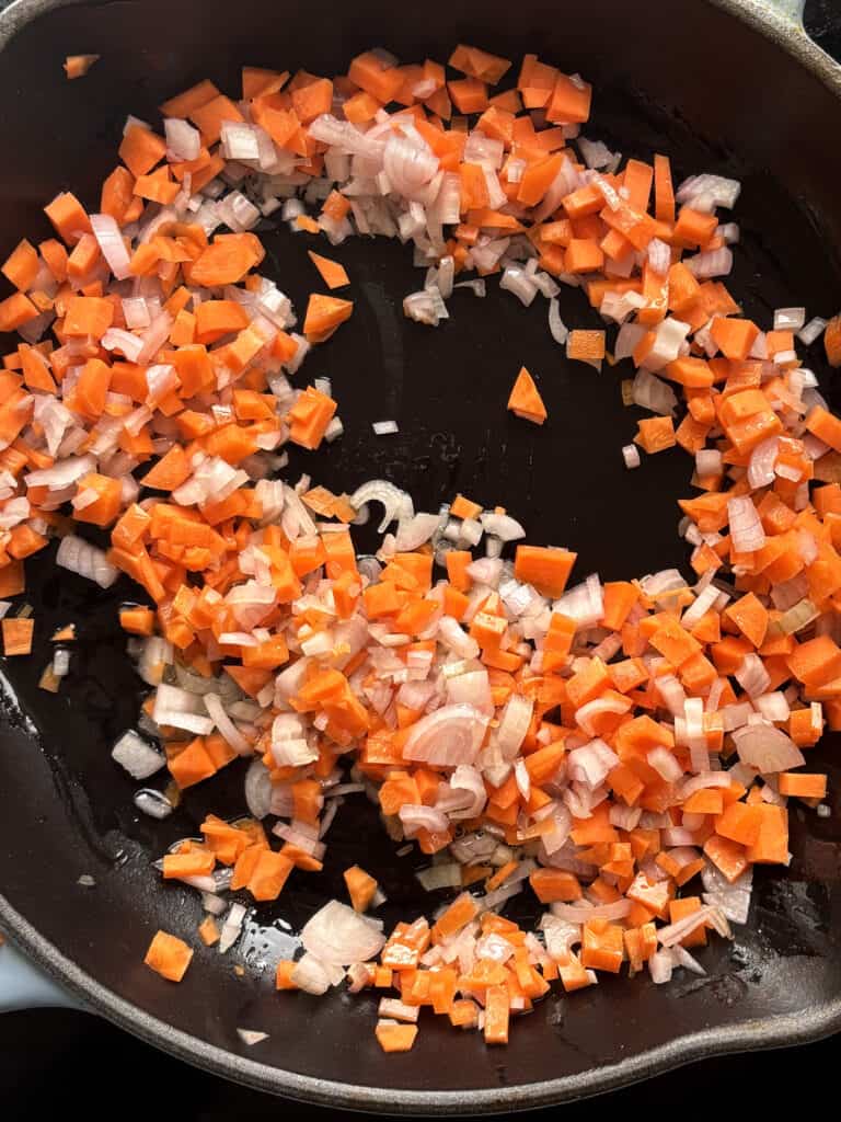 a skillet with diced onion, carrot and garlic cooking