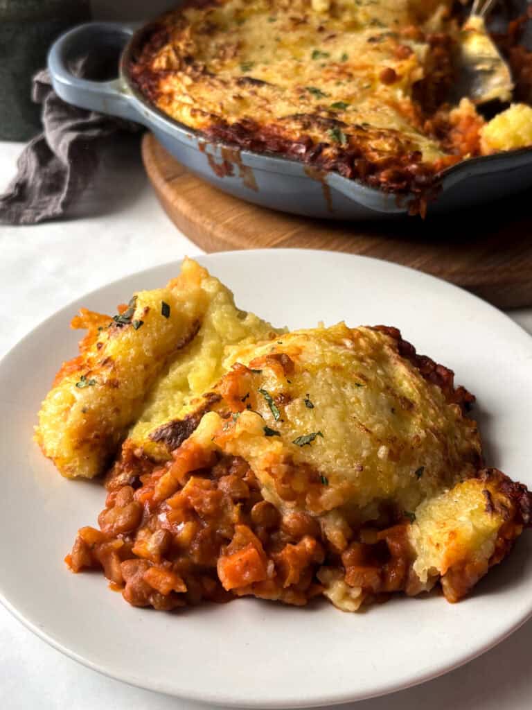 a white plate of vegetarian shepherd's pie with the full pan in the background