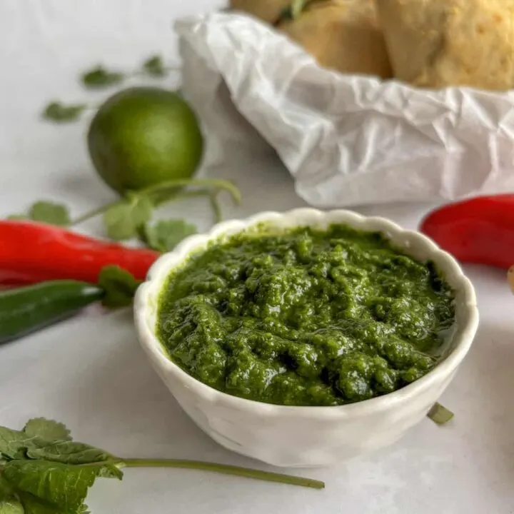 white bowl of mint and coriander chutney with samosas in the background