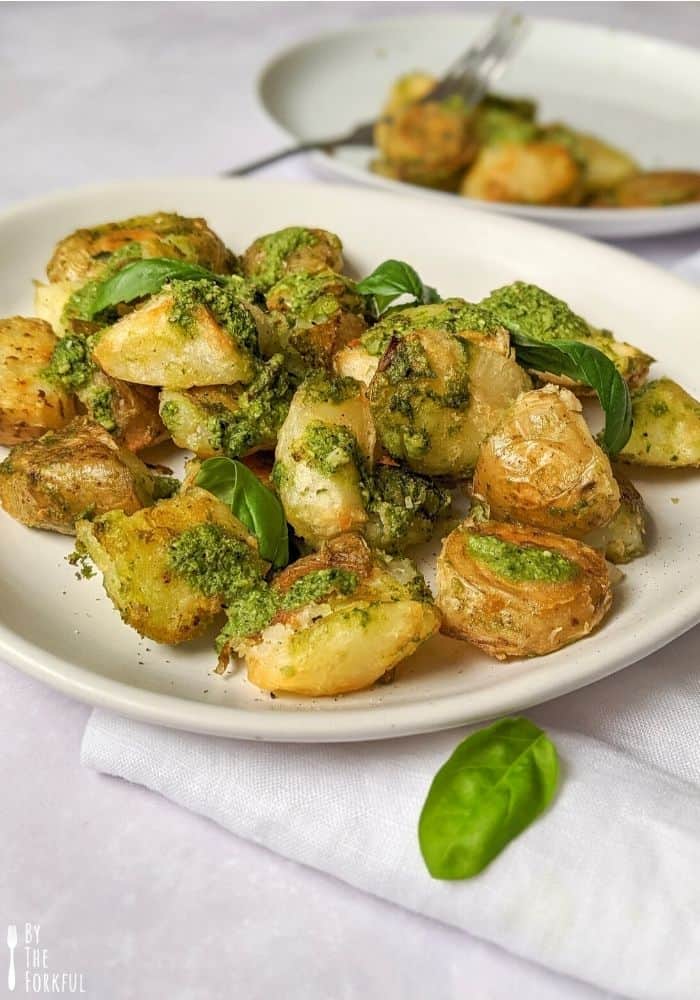 Pesto roasted potatoes on a white plate topped with fresh basil