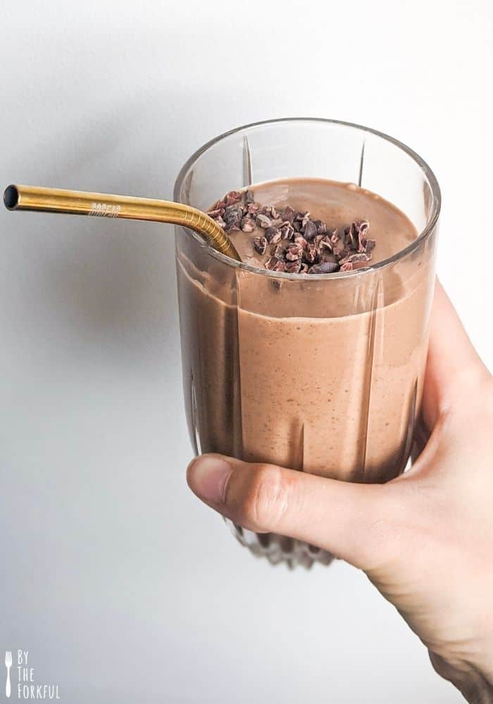 Photo of a chocolate pregnancy smoothie in a glass, with a golden metal straw. The smoothie is topped with cacao nibs.