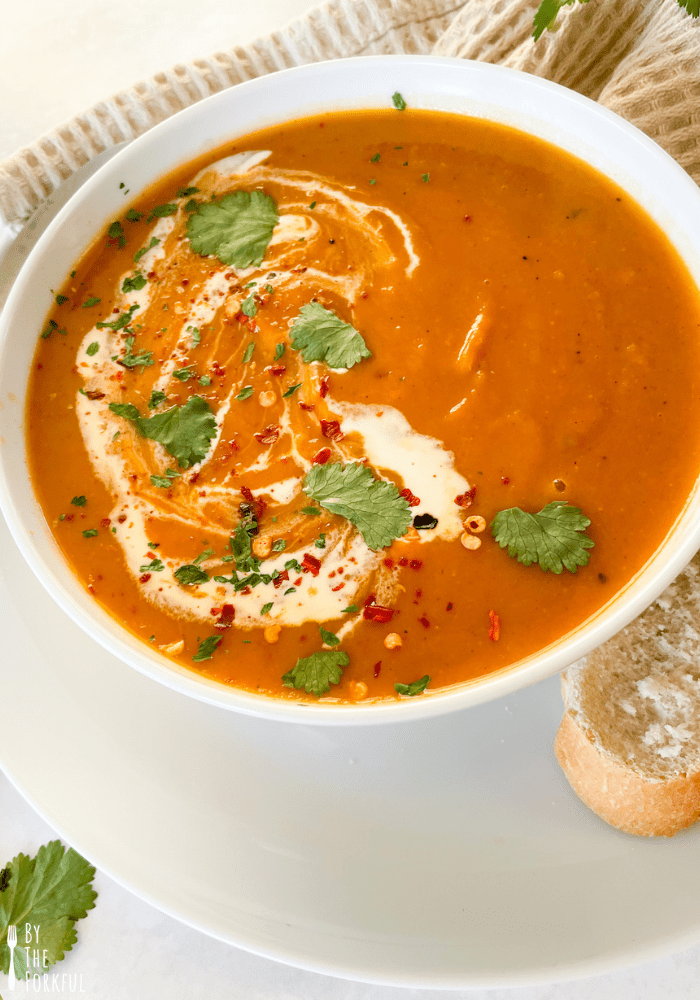 A close-up of buttetnut sqaush and sweet potato soup topped with vegan cream and chilli flakes.