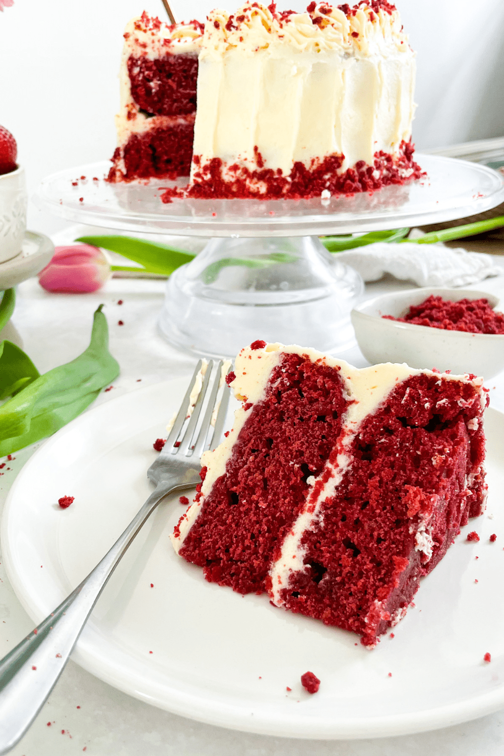 vegan red velvet cake slice on a plate, with the rest of the cake in the background