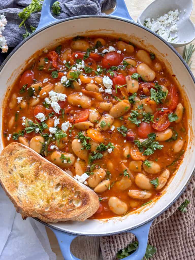 a casserole dish of butter bean stew with crusty bread on the side, topped with crumbled feta and parsely