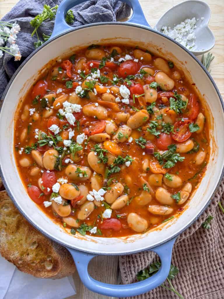 a casserole dish of butter bean stew with cherry tomatoes and lima beans topped with crumbled feta and parsely