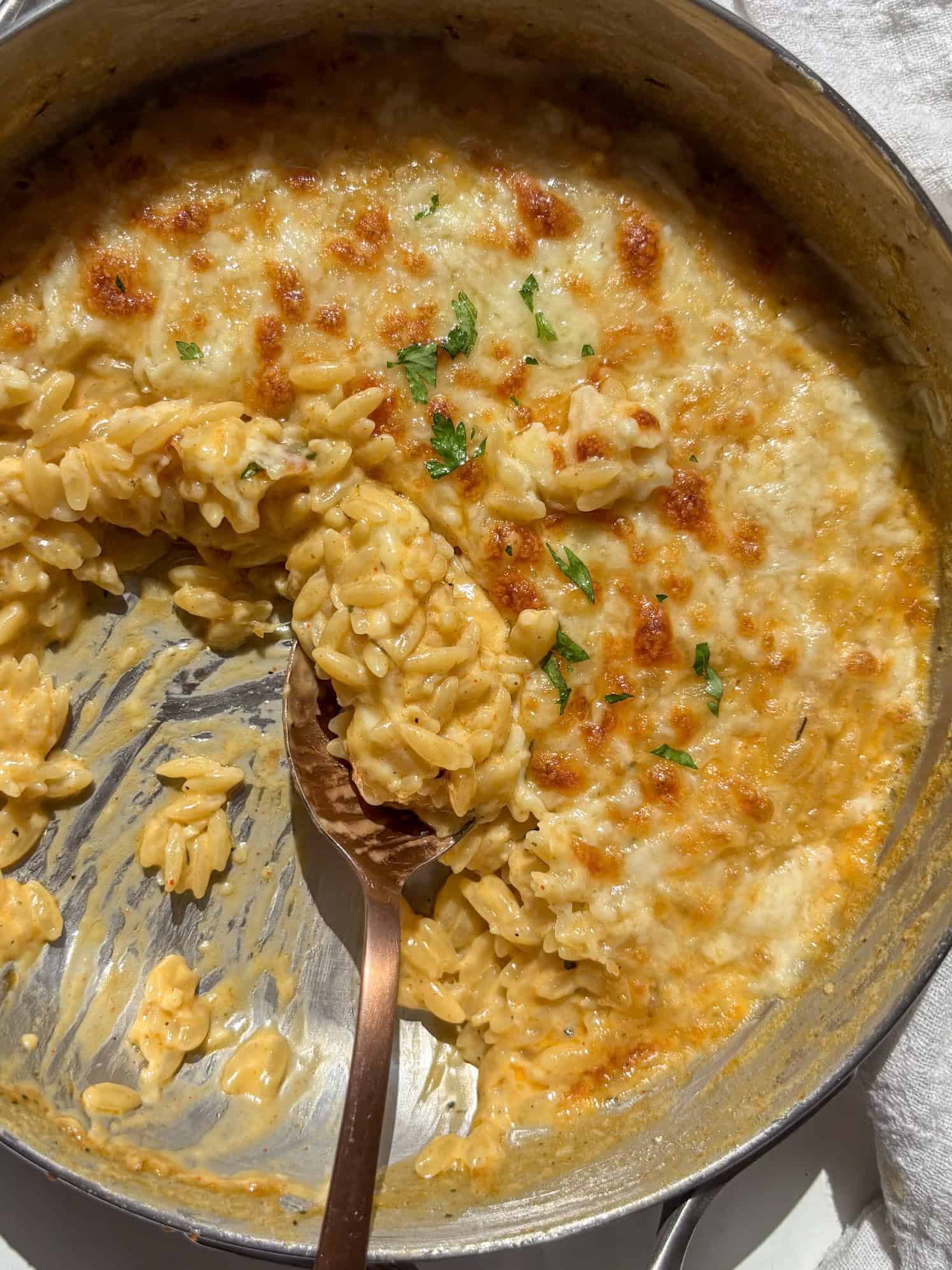 the golden and cheesy orzo mac and cheese with a portion taken out of the pan, a spoon in the pan taking a scoop