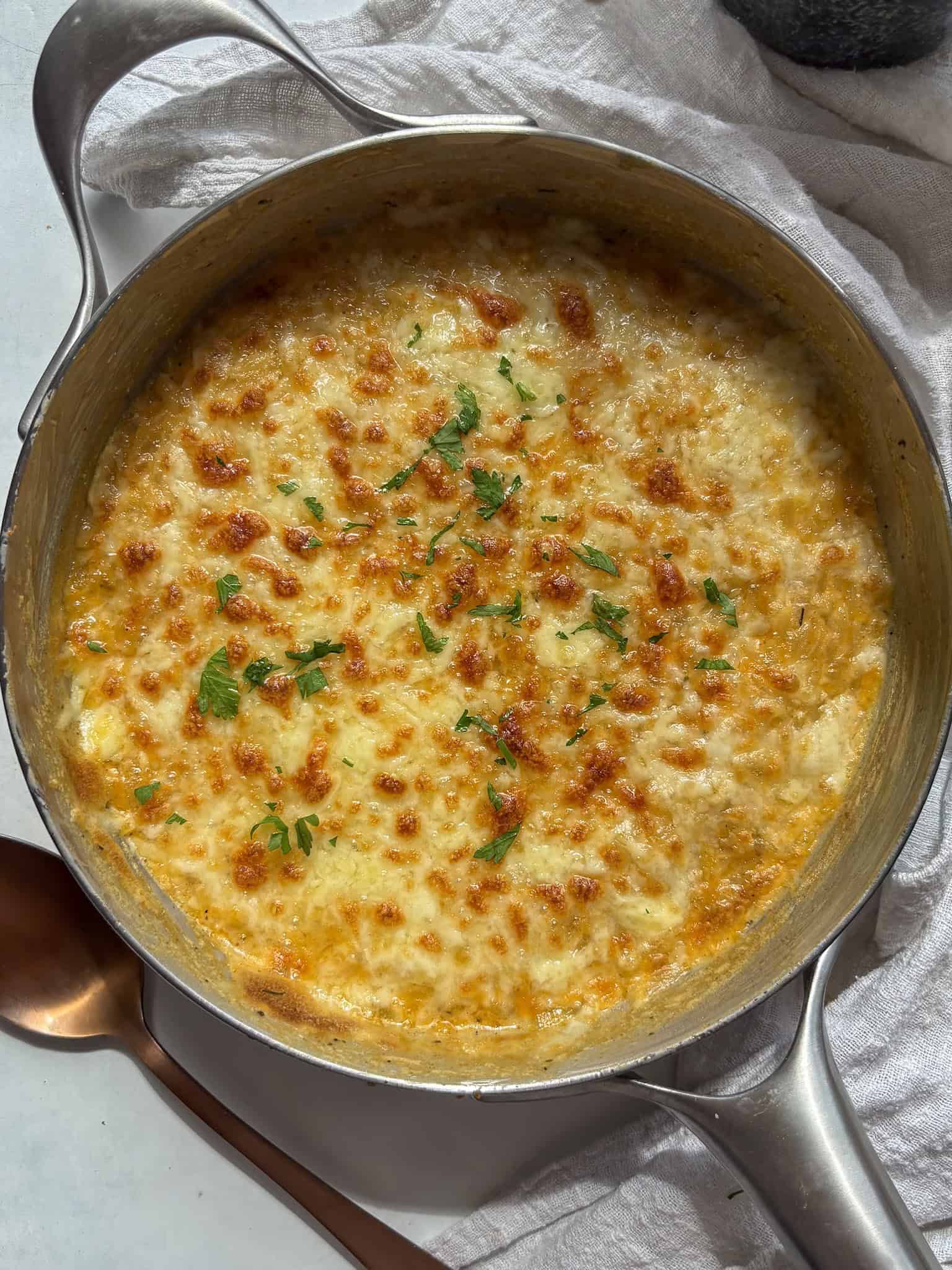 a skillet of golden and bubbly orzo mac and cheese topped with fresh herbs