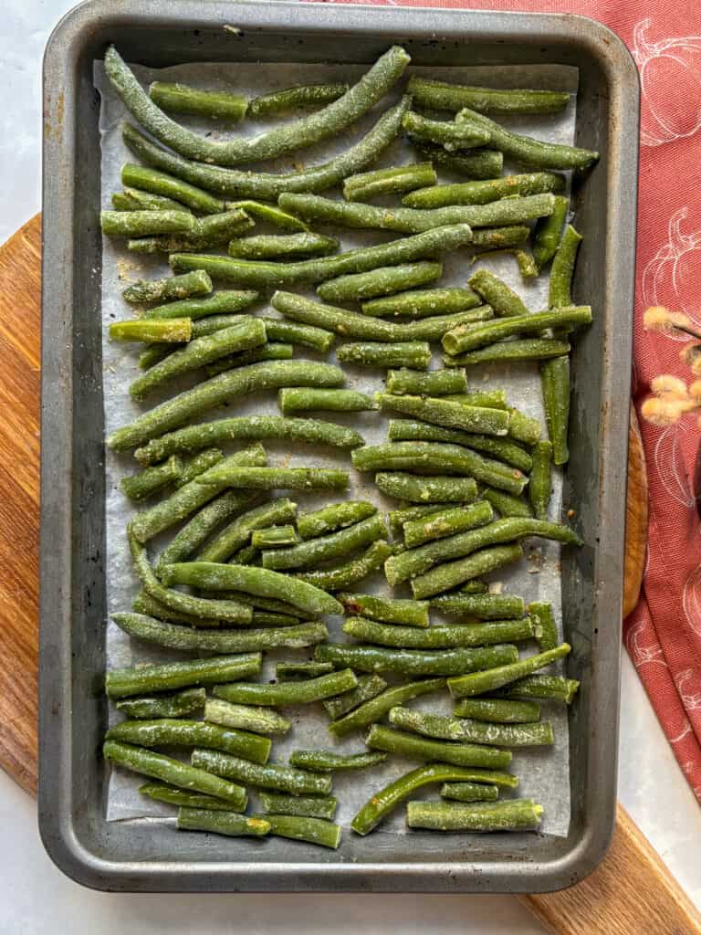 frozen green beans drizzled with oil and seasonings and arranged flat on a baking tray, ready to be roasted