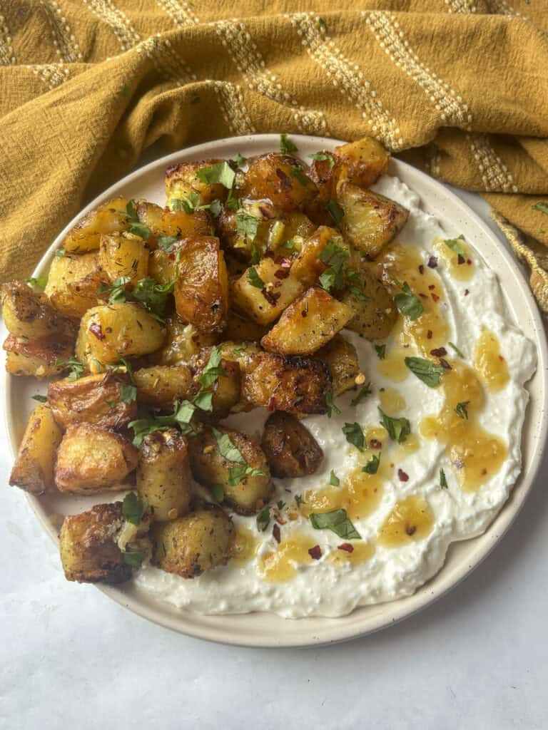 a plate of greek roasted potatoes on top of whipped feta while a roasted lemon, chili flakes and honey sauce