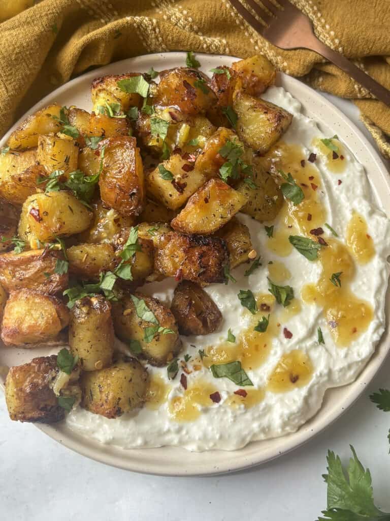 a plate of greek roasted potatoes on top of whipped feta while a roasted lemon, chili flakes and honey sauce