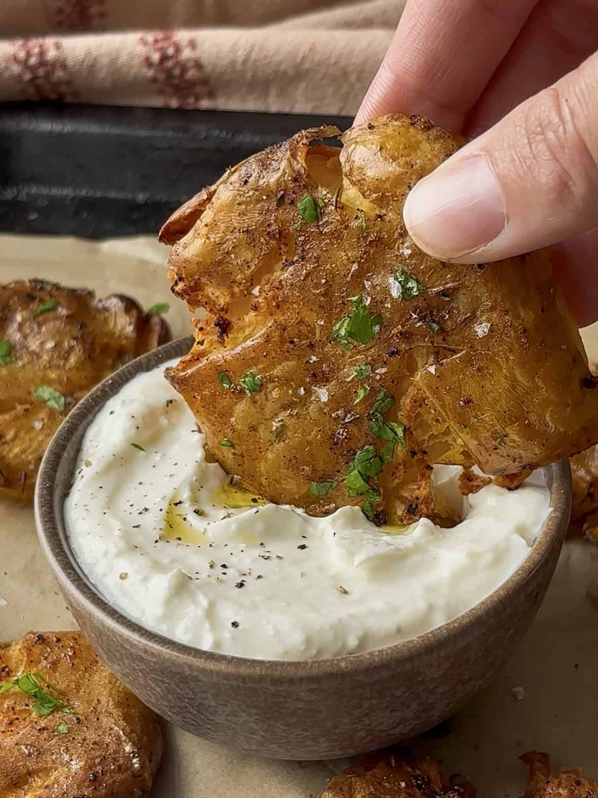 a crispy smashed potato being dipped into a lemon and garlic dip