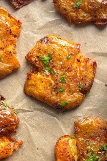 a baking sheet of smashed potatoes topped with flaky salt and fresh parsley