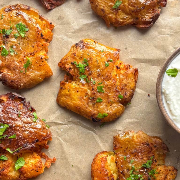 a baking sheet of smashed potatoes topped with flaky salt and fresh parsley