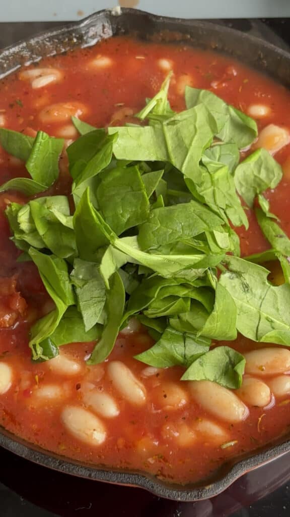 cheesy white bean tomato bake with fresh spinach added to the pan