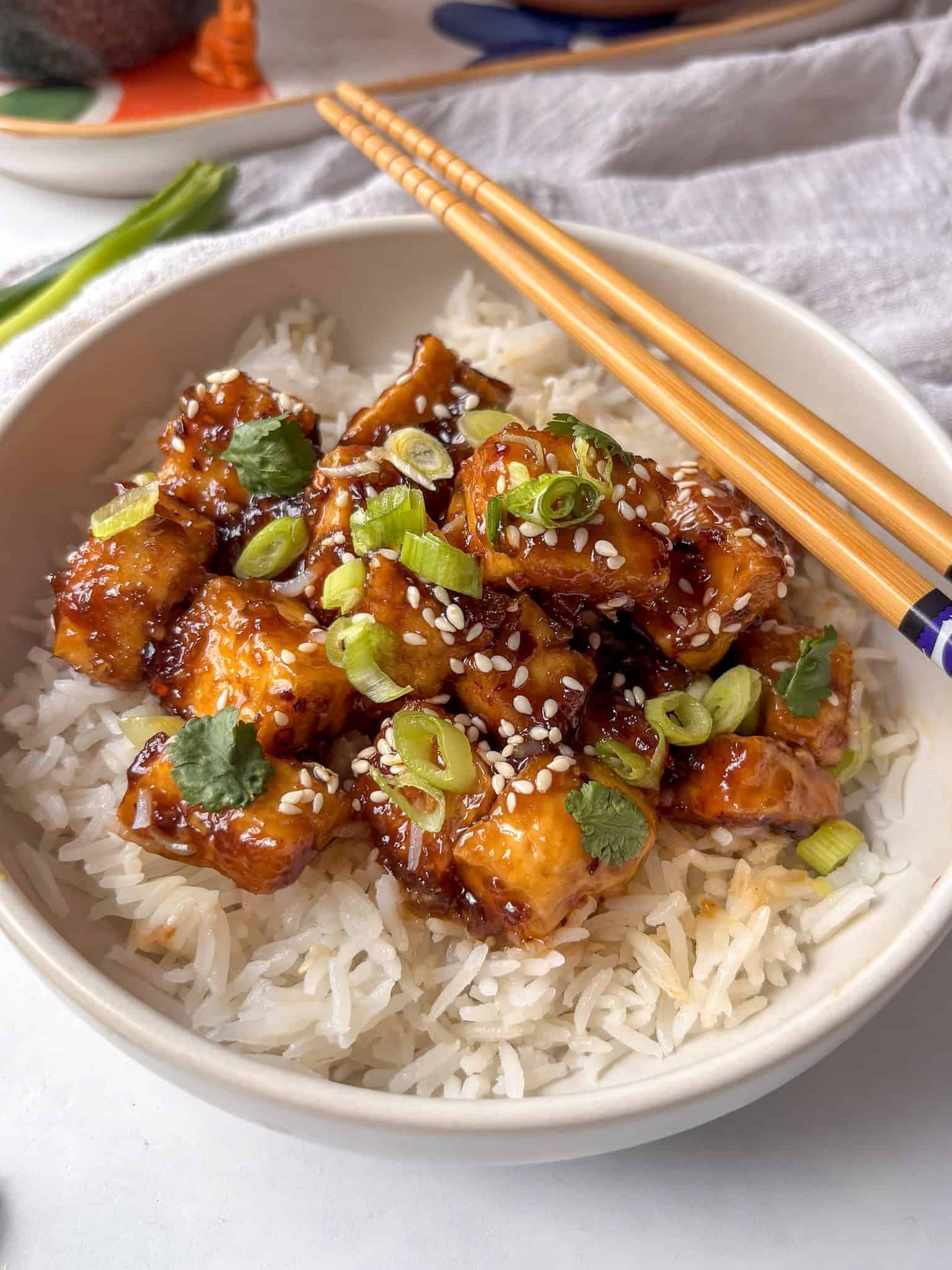 honey garlic tofu on top of rice, with scallions and sesame seeds on top