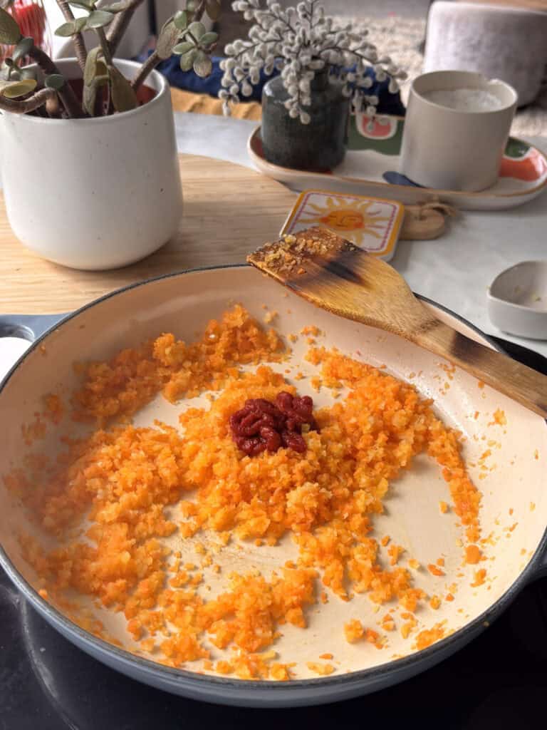 minced garlic added to the pan and stirred in, along with tomato paste about to be stirred into the soffrito base