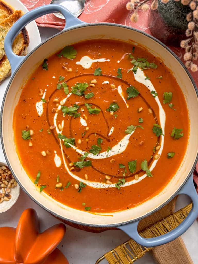 a pan of roasted butternut squash and red pepper soup, drizzled with extra virgin olive oil, cream, parsley, and toasted pine nuts on top