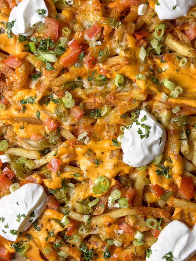 close up shot of epic loaded dirty fries with hot sauce, cheese sauce, jalapenos, sour cream, and diced tomato