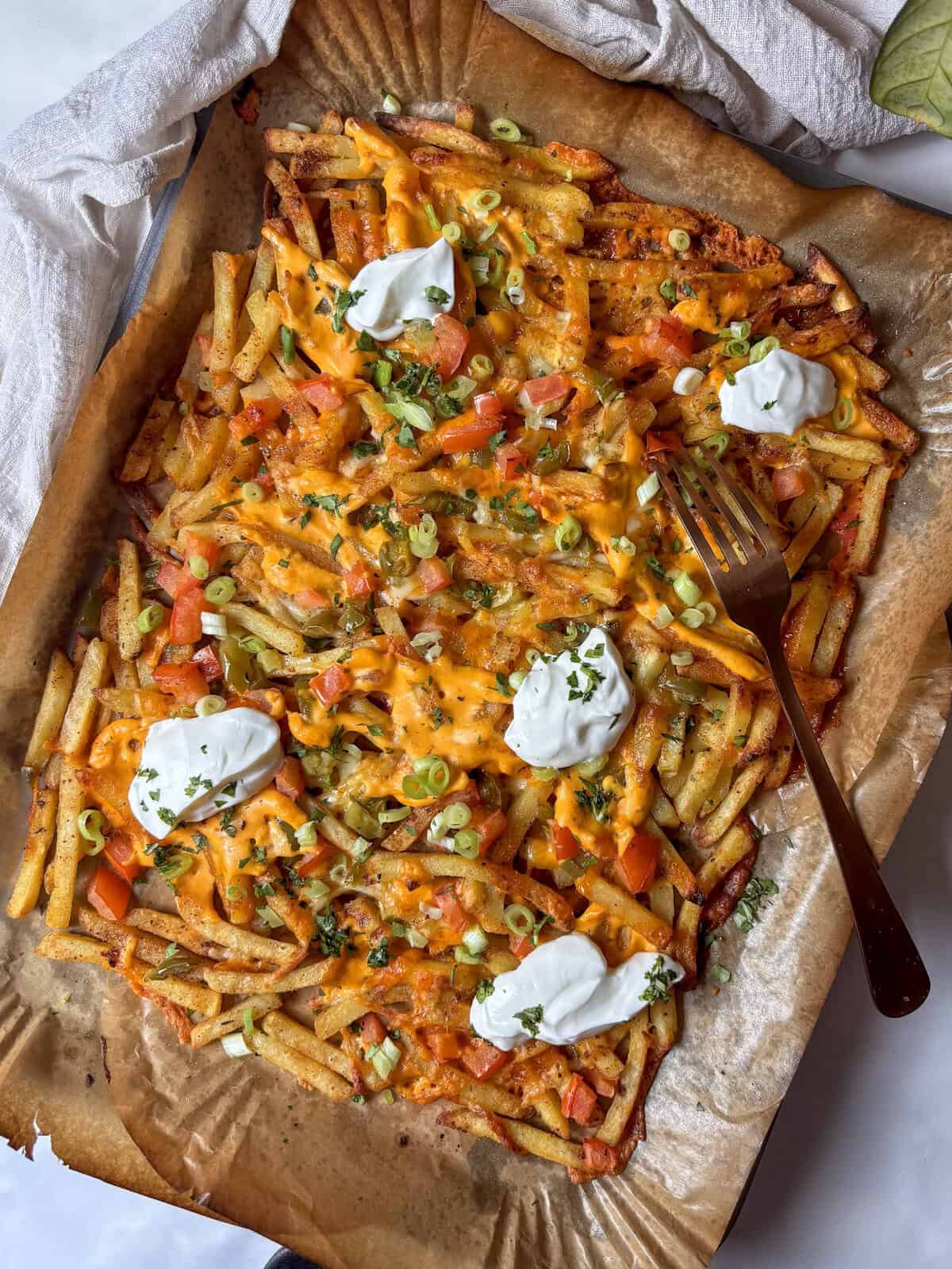 loaded dirty fries on a baking tray with sour cream, jalapenos, spring onion, buffalo sauce, and diced tomatoes