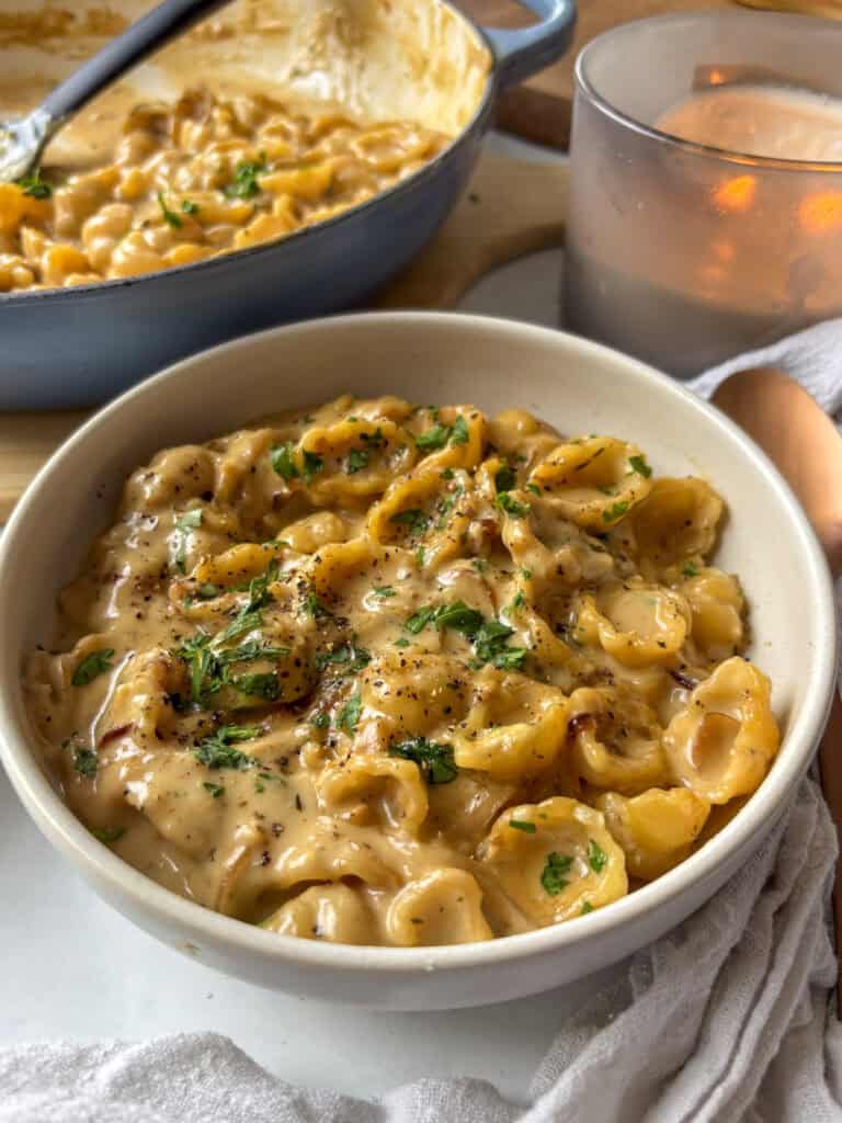 a bowl of creamy french onion pasta topped with black pepper and fresh herbs