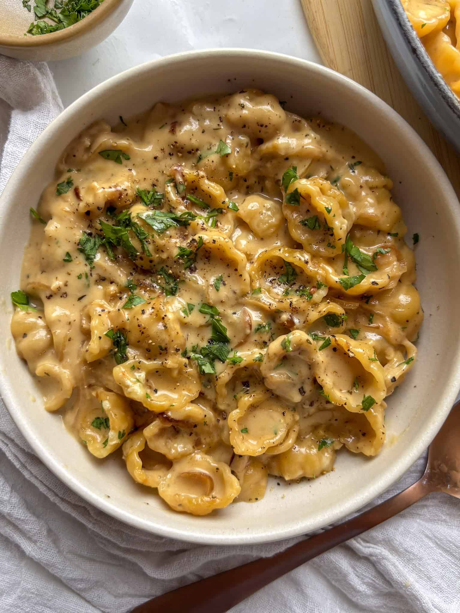 a bowl of cozy French onion pasta, topped with parsley and black pepper.