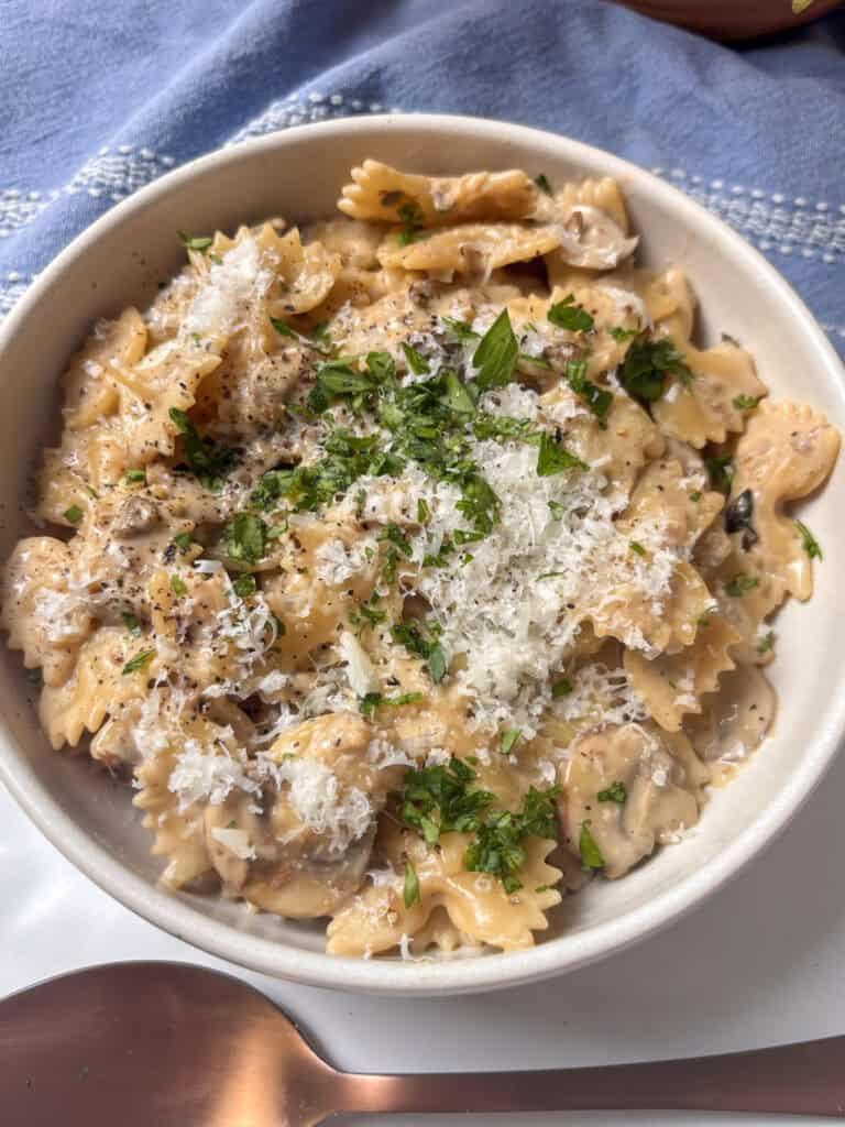 bowl of creamy mushroom pasta with bow pasta, pecorino cheese, and diced parsley