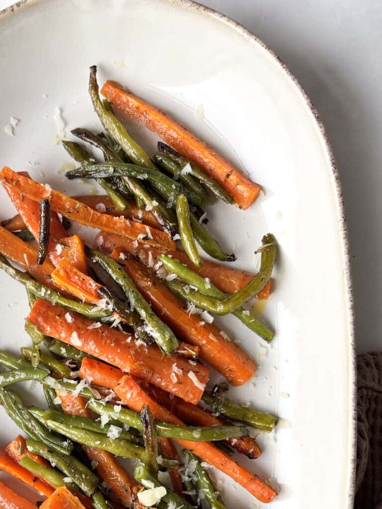 a close up shot of a serving dish with roasted green beans and carrots topped with Pecorino cheese and lemon zest