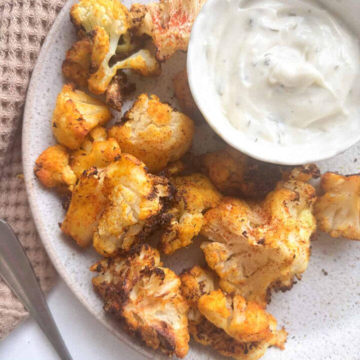 air fryer seasoned cauliflower on a serving plate with a small dipping bowl of garlic and herb sauce