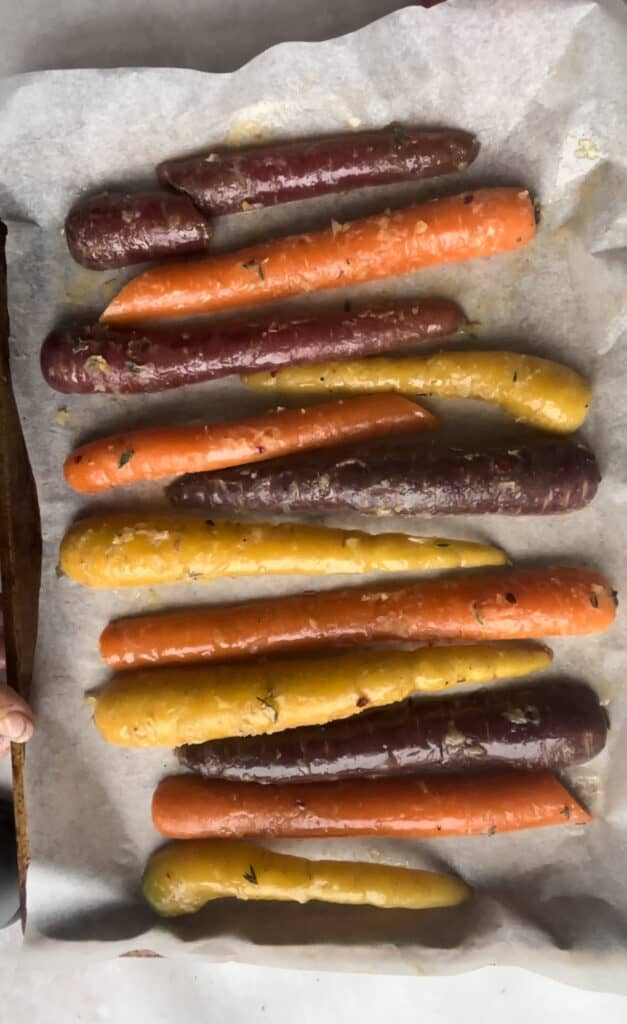 rainbow carrots coated in honey garlic butter sauce arranged neatly in rows on a baking tray lined with baking paper.