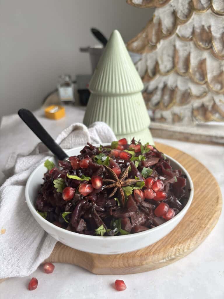 braised red cabbage in a white bowl topped with pomegranates and parsley. There is a star anise in the centre of the red cabbage bowl.