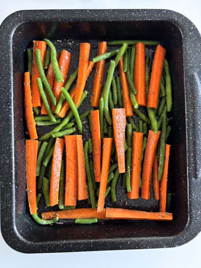 green beans and carrots coated in seasonings and olive oil and arranged neatly in a roasting dish