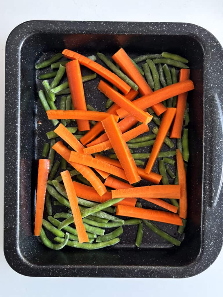 raw carrots and green beans in a roasting dish