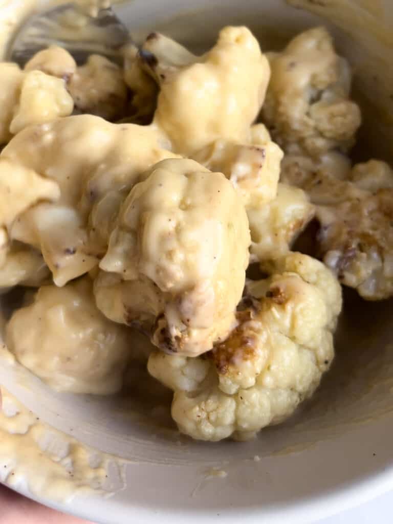 roasted cauliflower tossed in the cheese sauce in a mixing bowl
