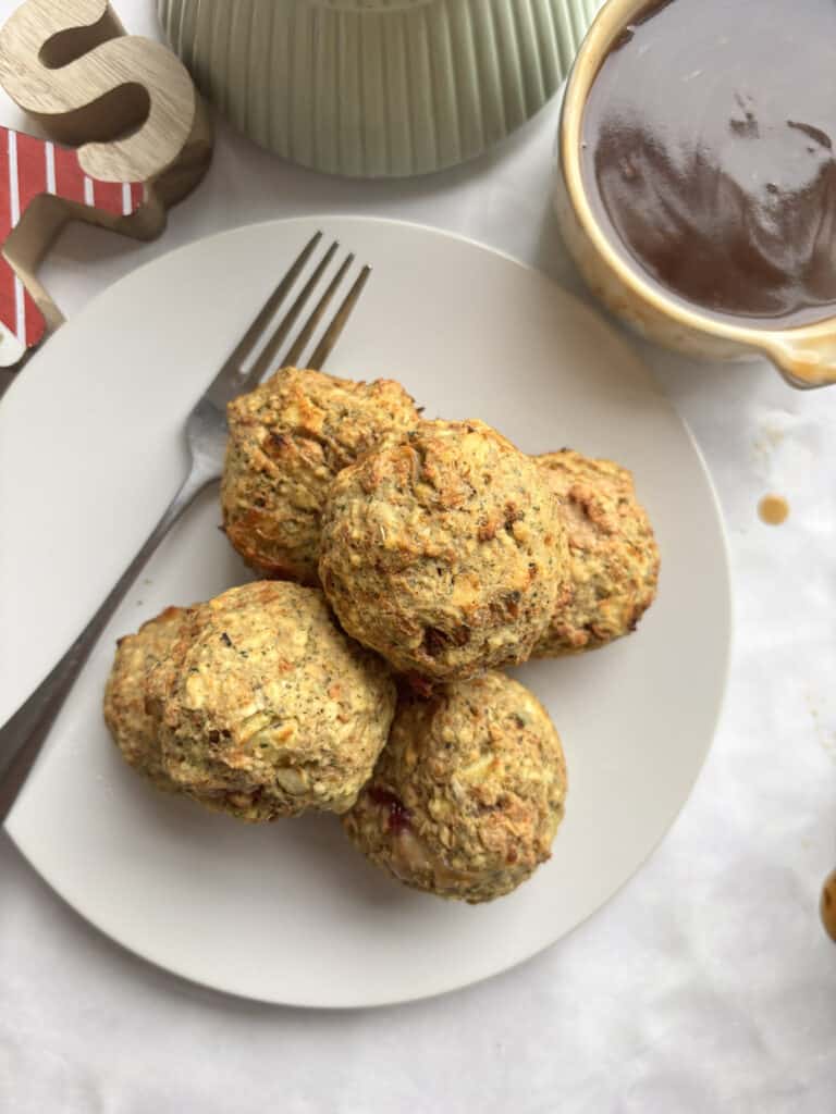 an overhead shot of six vegetarian stuffing balls on a white plate. There is also a bowl of gravy in the righthand corner of the photo.