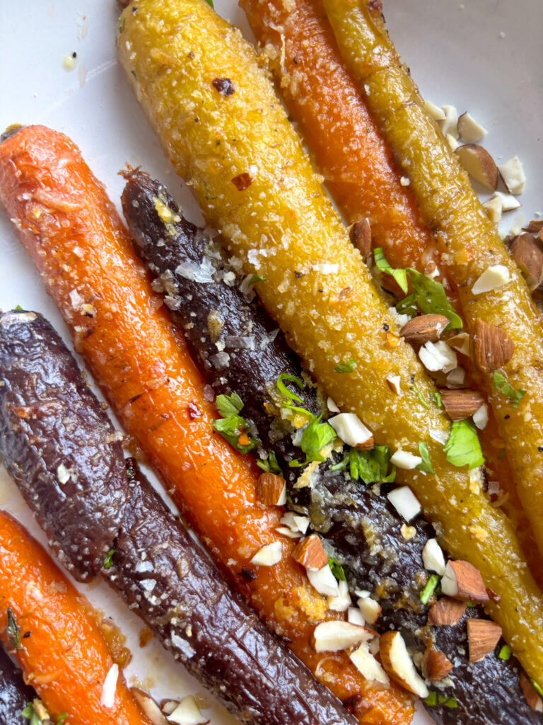 a very close up shot of a serving plate of rainbow honey butter carrots topped with fresh parsley and chopped almonds