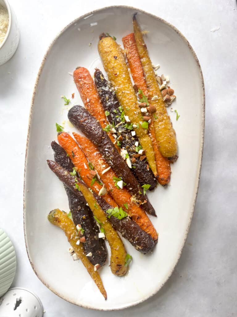 a serving plate of rainbow honey butter carrots topped with fresh parsley and chopped almonds