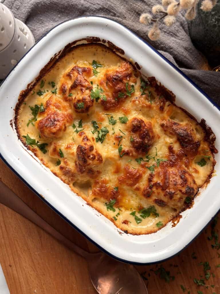 overhead shot of cauliflower cheese with a golden crispy topping and fresh parsley scattered on top