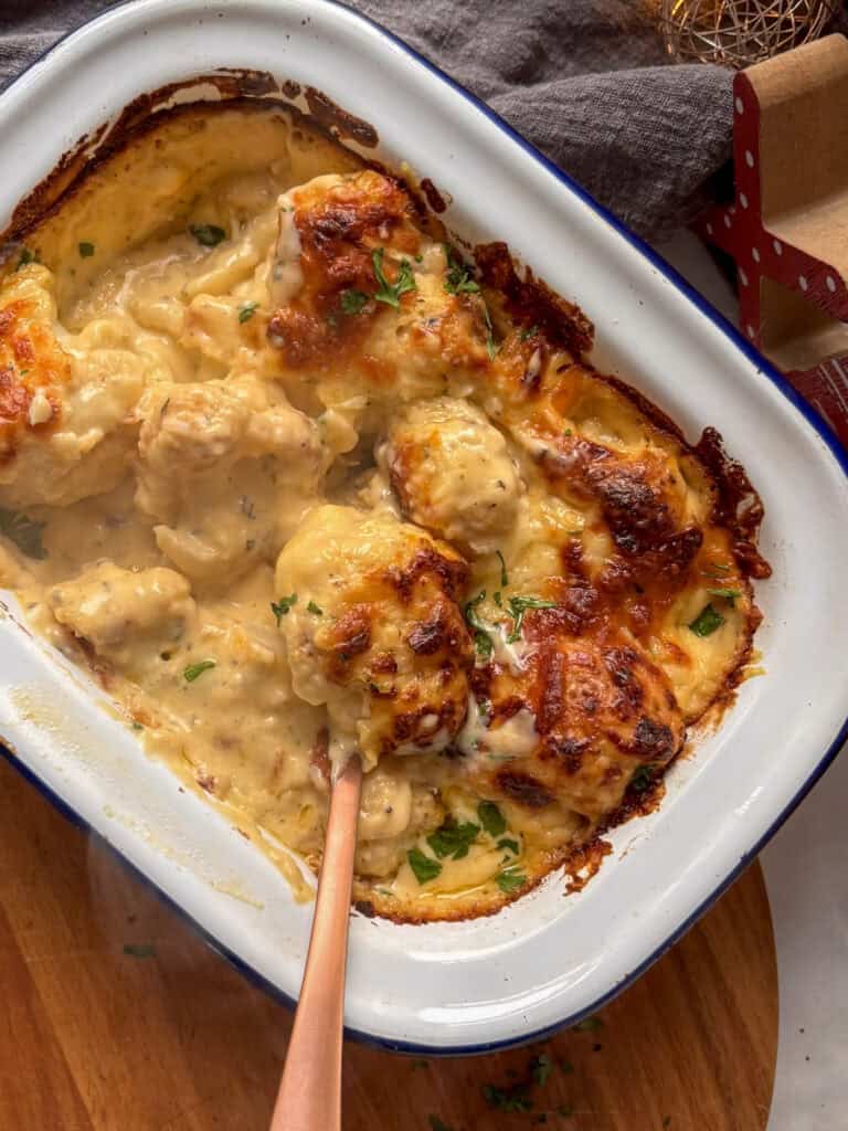 the finished cauliflower cheese with a scoop taken out of it - the bubbling cheese topping partially shown