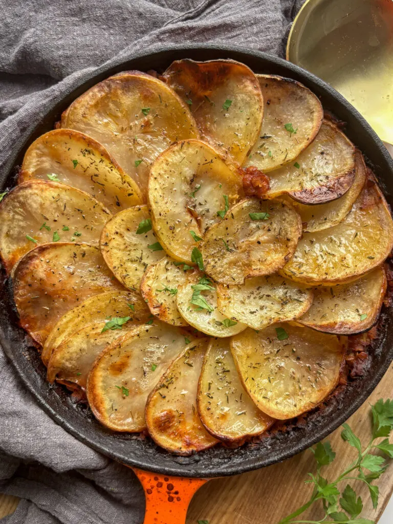 an overhead shot of a vegan lentil hotpot topped with golden crispy potato slices. The hotpot is cooked in a cast iron skillet.