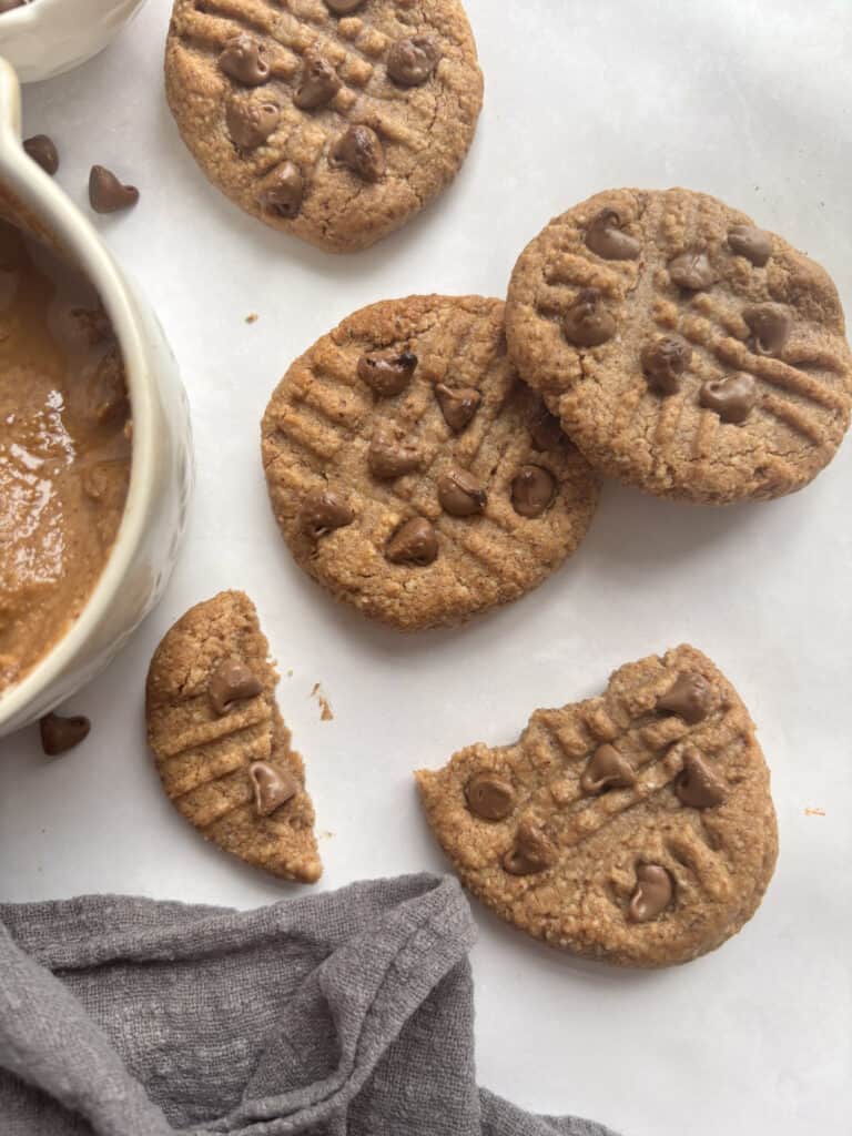A selection of almond butter cookies on a white background. One cookie is broken in two.