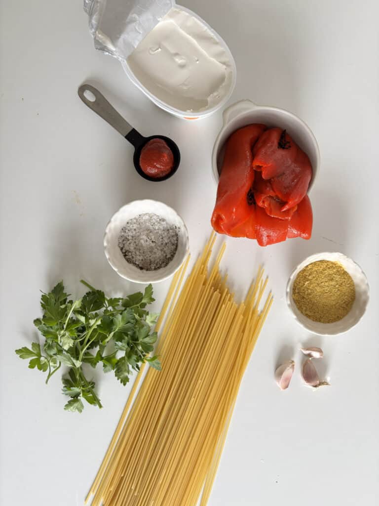 the roasted red pepper pasta ingredients: spaghetti, roasted red peppers, garlic, nutritional yeast, parsley, salt, pepper, tomato puree, and cream cheese