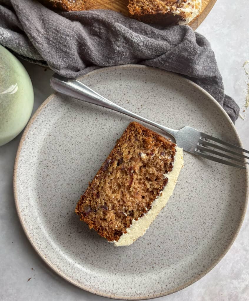 a slice of vegan applesauce cake on a speckled grey plate, with a silver fork next to it.
