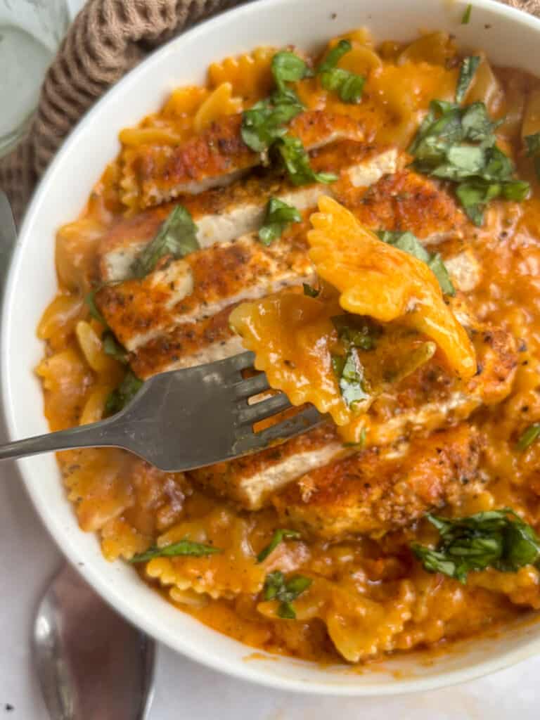 a close up shot of the marry me bow-tie pasta on a fork. The rest of the bowl is slightly blurred out in the background